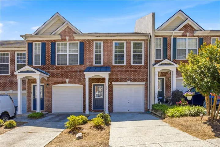 Brick facade townhome featuring white garage doors, blue accent shutters, covered entryways, and concrete driveways