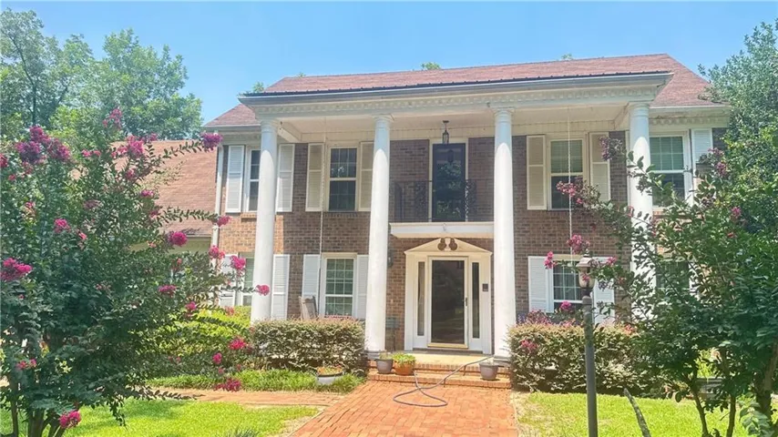 Brick exterior with a covered entry featuring white columns, a second-story balcony with an ornate iron railing, white window shutters, and a brick pathway