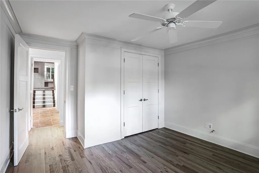 Unfurnished bedroom featuring dark wood-type flooring, a closet, a ceiling fan, and crown molding