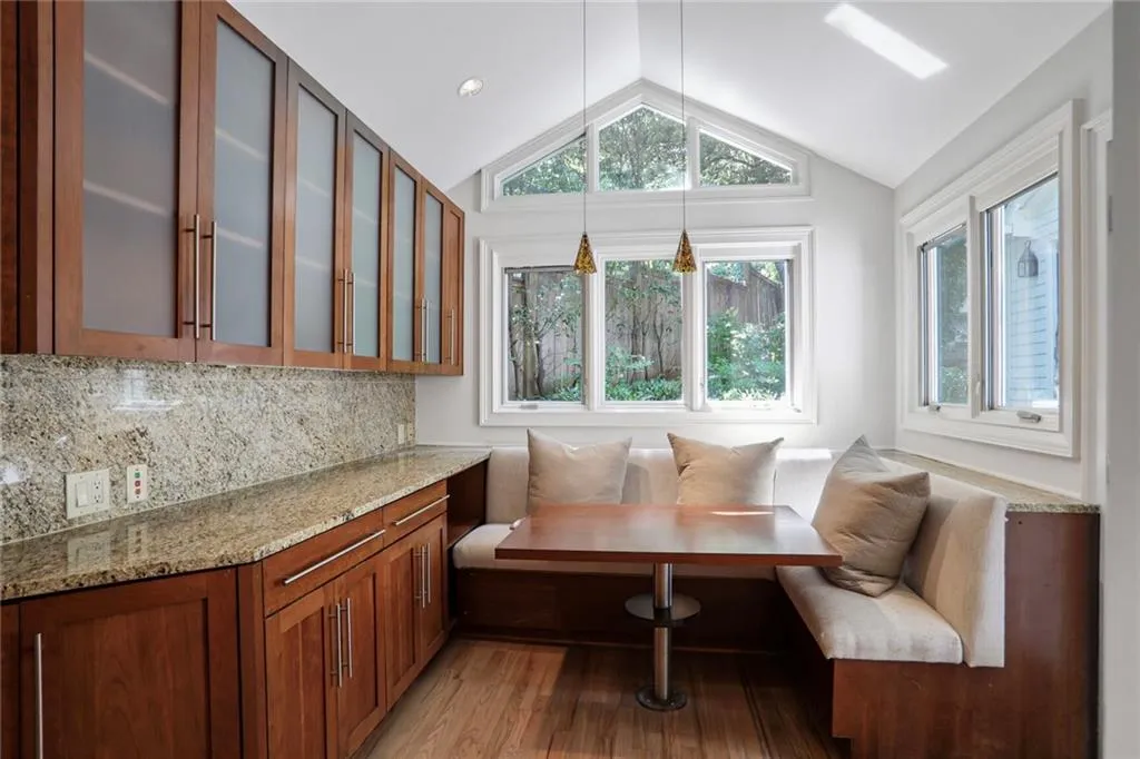Kitchen featuring light wood-style flooring, lofted ceiling, light stone counters, brown cabinets, and glass insert cabinets