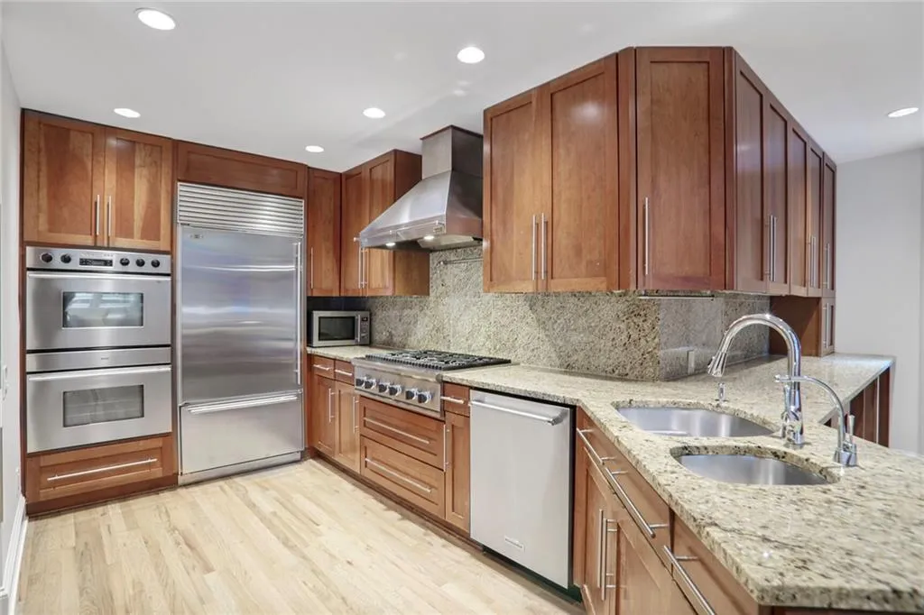 Kitchen with appliances with stainless steel finishes, wall chimney range hood, tasteful backsplash, light stone counters, and recessed lighting