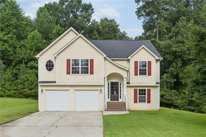Split-level residence featuring a two-car garage, red louvered shutters, a dark shingle roof, an arched entry portico, and a prominent oval window
