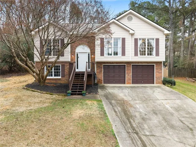 Two-story brick and siding residence featuring a two-car garage with dark brown doors, a covered entry portico with white trim, and multi-pane double-hung windows