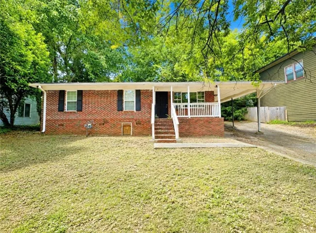 Brick facade residence featuring a covered front porch, white railing, and a carport
