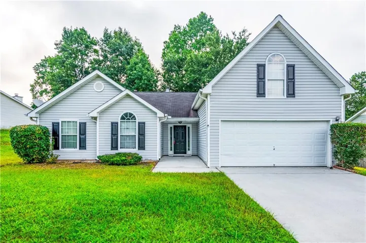 Light gray siding exterior with dark shutters, arched windows, attached garage, and concrete driveway
