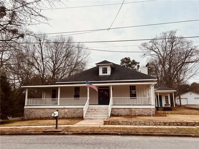 View of front facade with board and batten siding, a detached garage, covered porch, a shingled roof, and a chimney