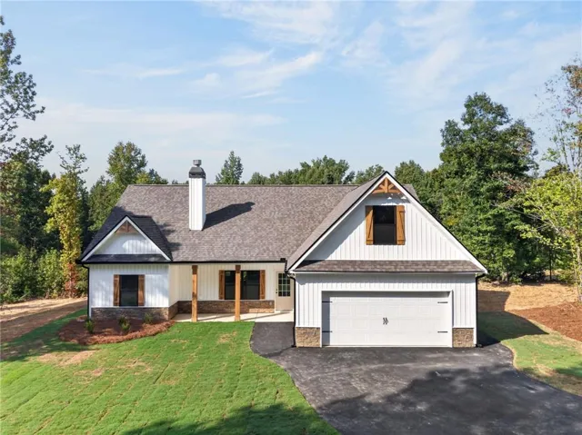 White board and batten siding with stone accents, covered front porch with wood columns, attached two-car garage, and a newly installed asphalt driveway
