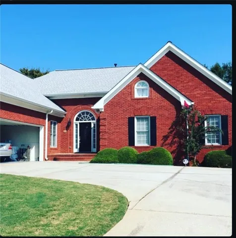 Red brick facade with a light-colored roof, featuring a prominent arched entry, white window trim, and dark shutters