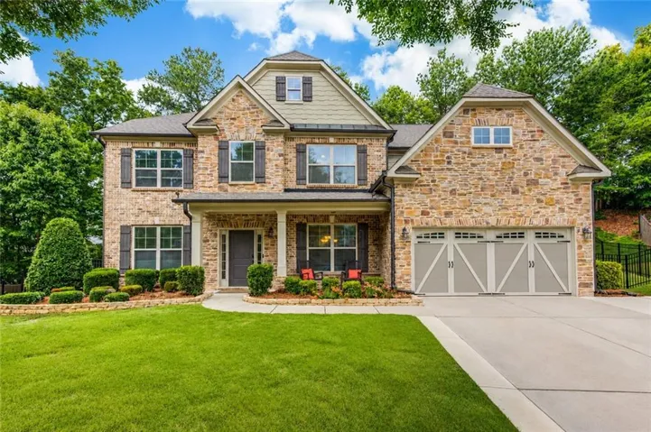Stone facade residence featuring a covered front porch, dark-paneled garage doors, and a concrete driveway