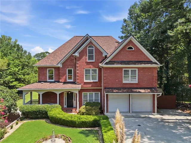 Brick exterior with a gabled roofline, covered front porch, attached two-car garage, and manicured landscaping