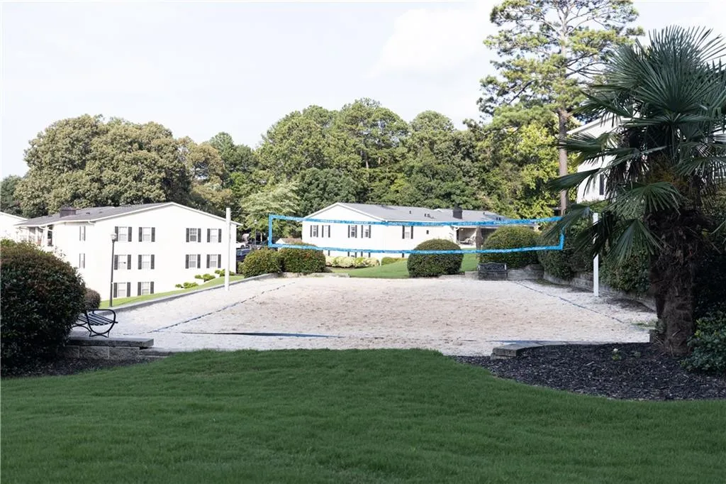 Sand volleyball court featuring a net, surrounded by manicured landscaping and mature trees