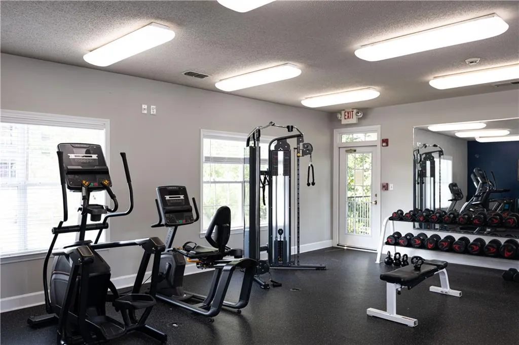 Dedicated fitness area featuring rubber flooring, extensive mirror wall, white trim windows, and a glass-paneled exterior door leading to a balcony