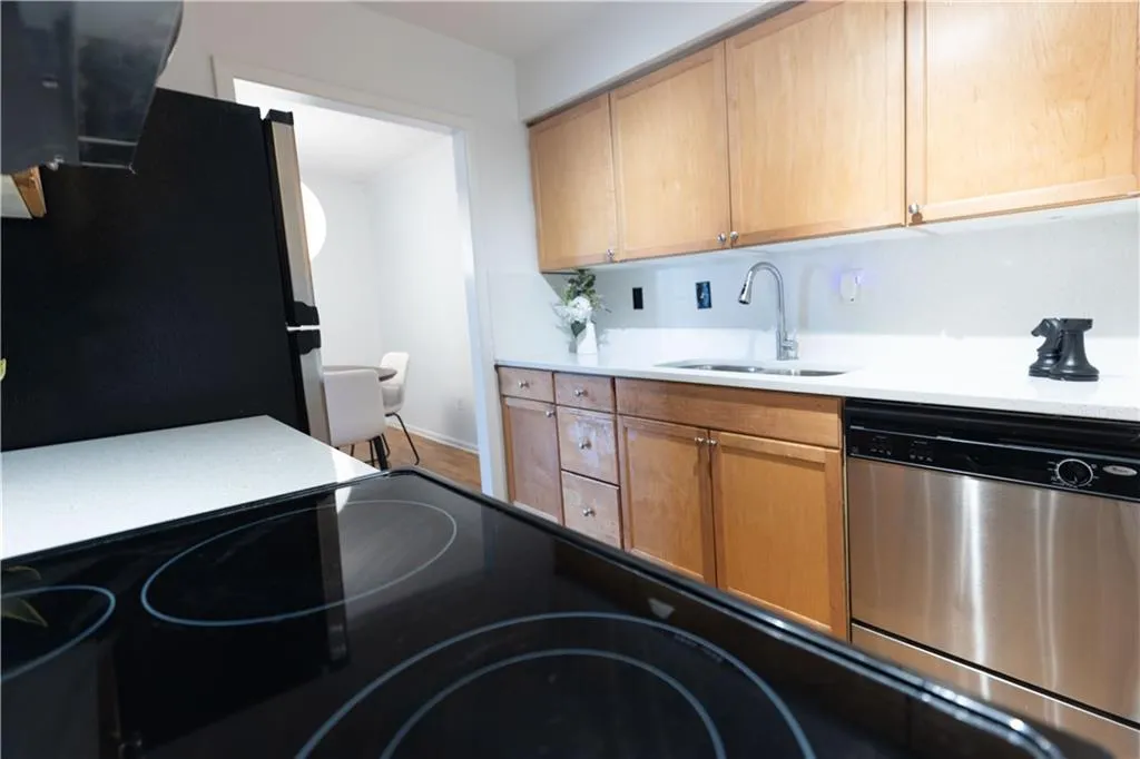 Kitchen featuring wood cabinetry, white countertops, stainless steel dishwasher, and a black electric cooktop
