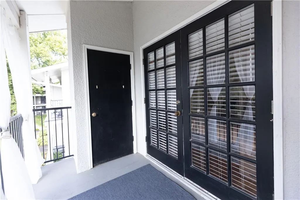 Exterior balcony with dark-paneled double doors featuring internal blinds and a black metal railing