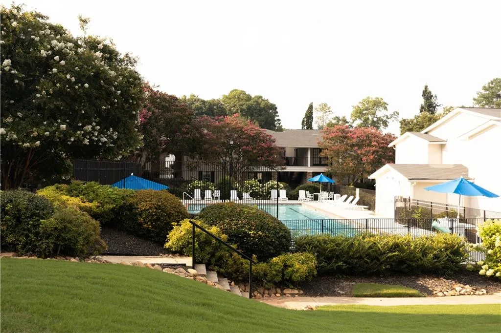 Community swimming pool featuring a black metal fence, ample lounge seating, and surrounding mature landscaping