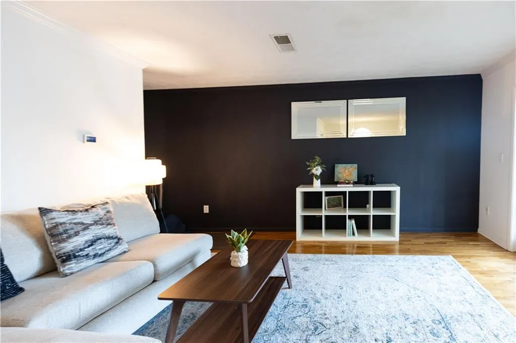 Spacious living area featuring light wood-finish flooring, a dark accent wall, and crown molding
