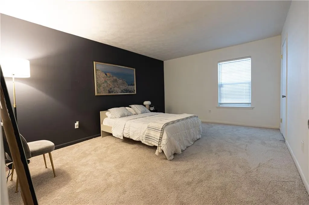 Expansive carpeted room featuring a window with horizontal blinds, a dark accent wall, and a white interior door