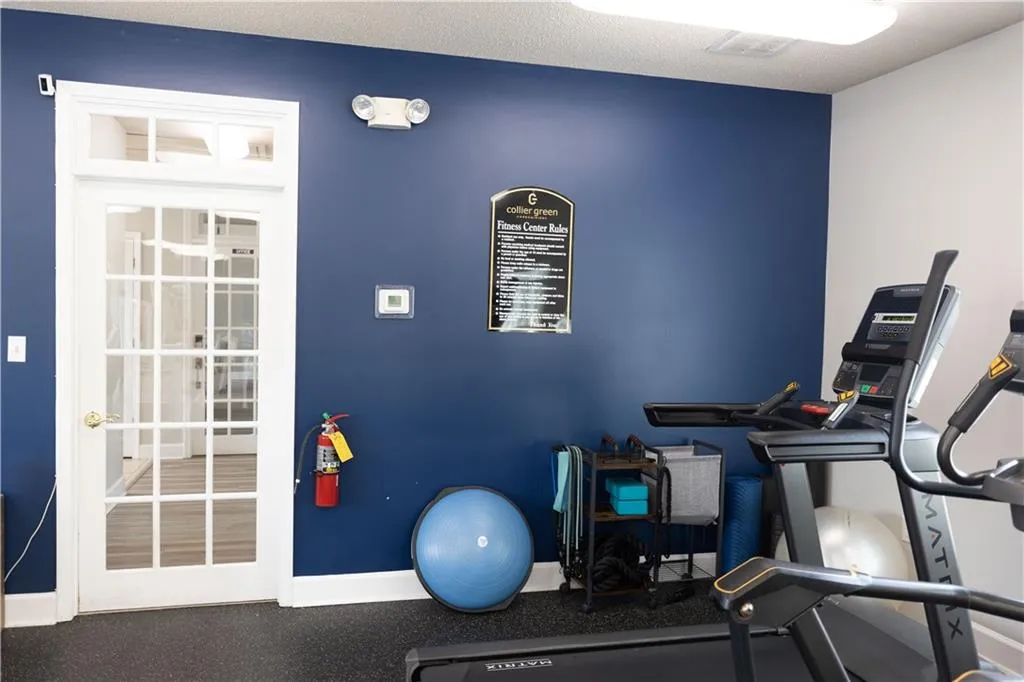 Fitness area featuring a paneled glass door with transom, dark blue accent wall, and rubber flooring