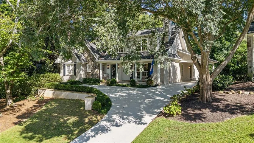 Brick and stone exterior, multi-pitch roof, arched entryways, extensive mature landscaping, and a curvilinear driveway