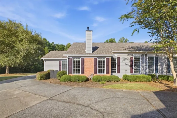 Exterior featuring gray siding, brick accents, multiple windows with shutters, and a prominent chimney
