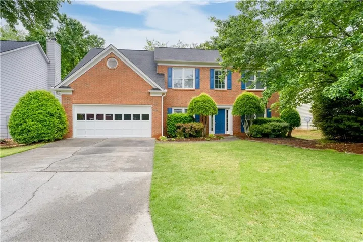 Brick façade residence featuring a two-car garage with panel windows, a vibrant blue entry door, and matching blue window shutters