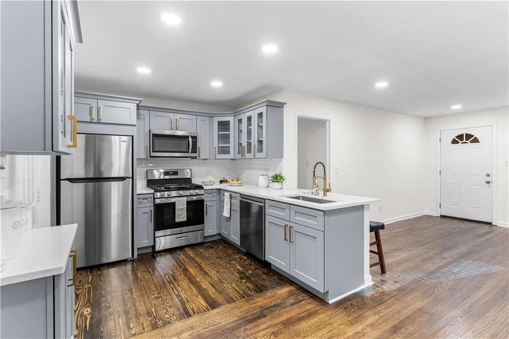 Kitchen featuring gray cabinetry, stainless steel appliances, glass insert cabinets, dark wood-style floors, and recessed lighting