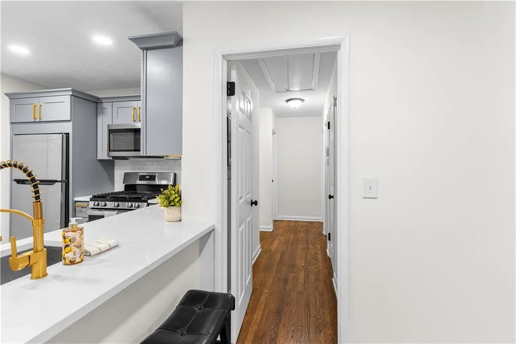 Kitchen with tasteful backsplash, dark wood finished floors, appliances with stainless steel finishes, gray cabinetry, and light stone countertops