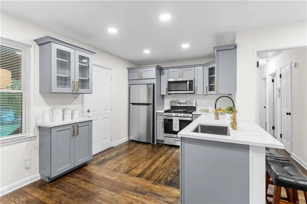 Kitchen featuring gray cabinetry, glass insert cabinets, stainless steel appliances, backsplash, and a kitchen bar