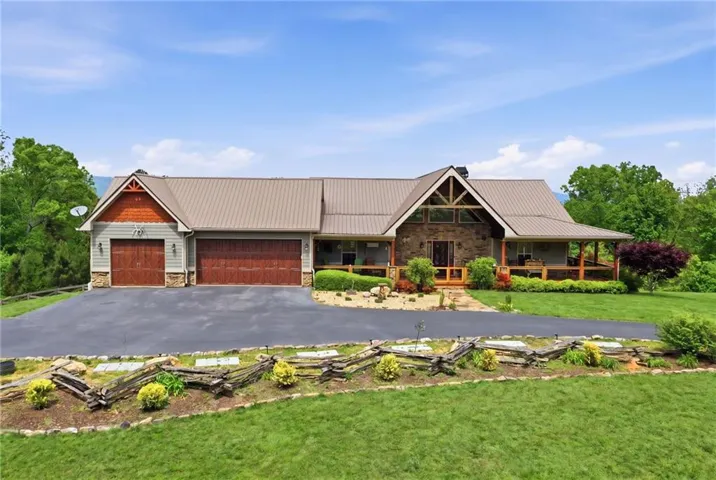Rustic-style home featuring a metal roof, stone facade, covered front porch, and an attached four-car garage with wood-finish doors