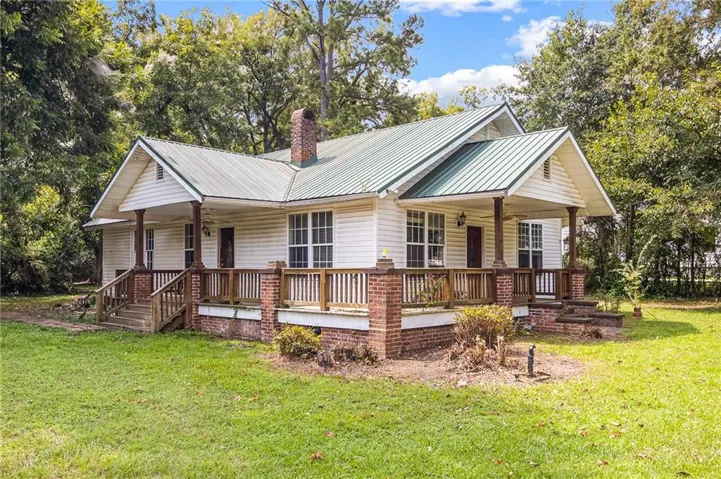 White siding exterior with a green metal roof, a brick chimney, and a covered front porch featuring wood columns and railing