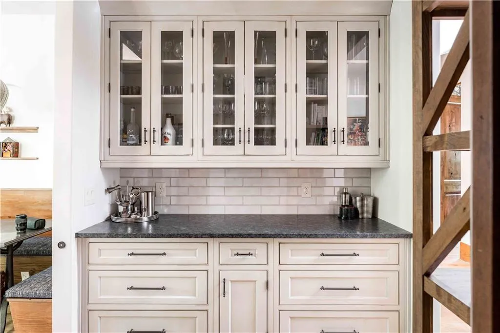 Bar featuring decorative backsplash, glass insert cabinets, and cream cabinets