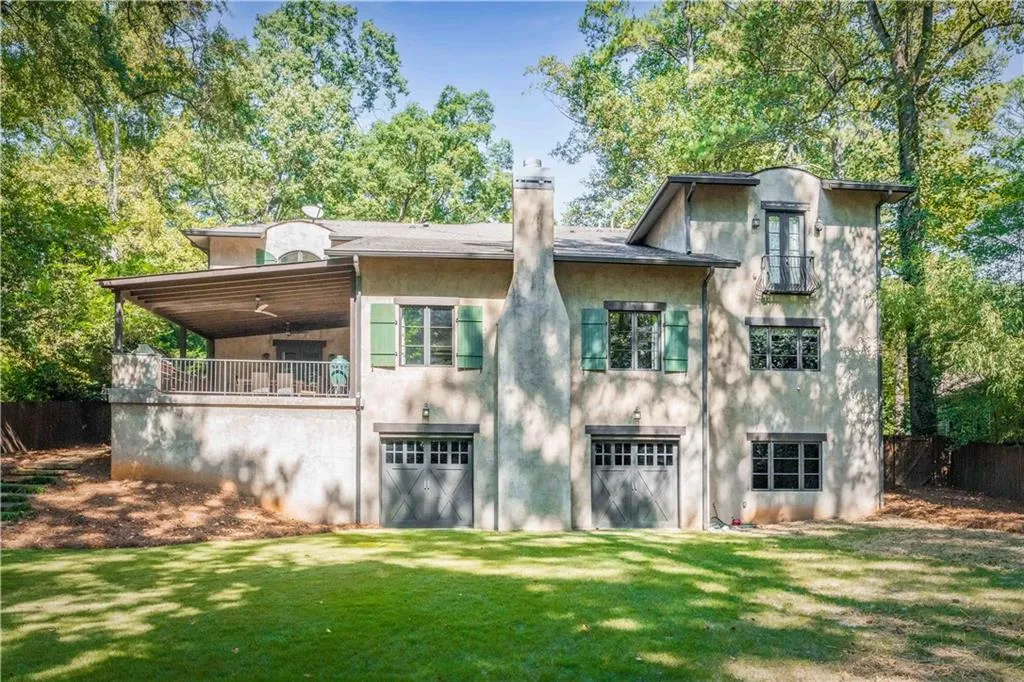 Back of property featuring a balcony, a lawn, a chimney, and stucco siding