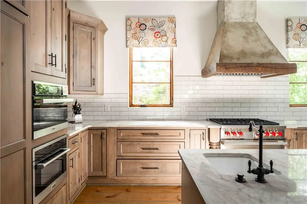 Kitchen with custom exhaust hood, light stone counters, tasteful backsplash, appliances with stainless steel finishes, and light brown cabinetry