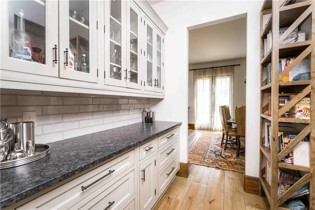 Bar featuring light wood-type flooring, decorative backsplash, glass insert cabinets, and white cabinetry