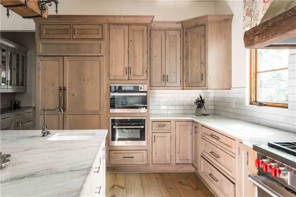 Kitchen featuring custom range hood, light stone countertops, stainless steel appliances, tasteful backsplash, and light wood-type flooring