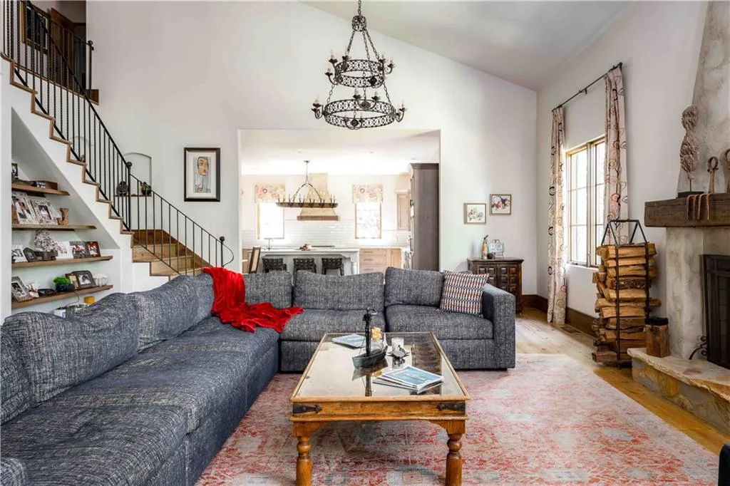 Living room featuring a fireplace with raised hearth, wood finished floors, a chandelier, vaulted ceiling, and stairway