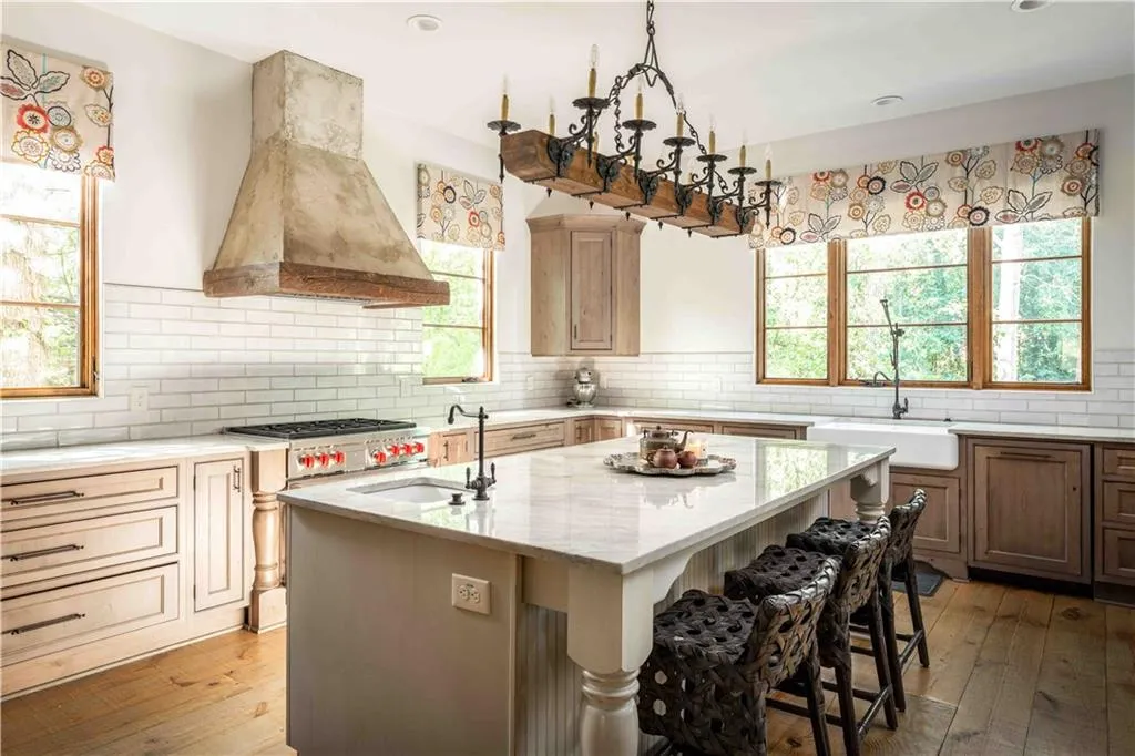 Kitchen with light wood-style flooring, premium range hood, light stone countertops, an island with sink, and backsplash