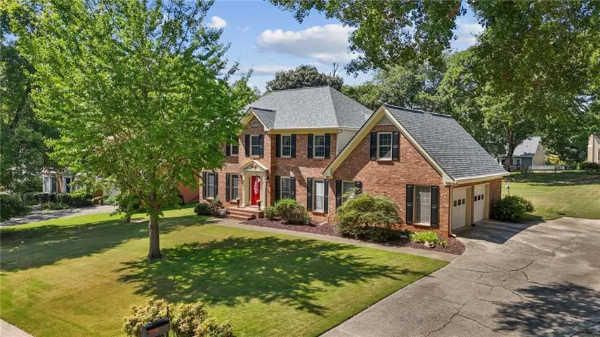 Brick exterior with black shutters, mature landscaping, two-car garage, and a concrete driveway