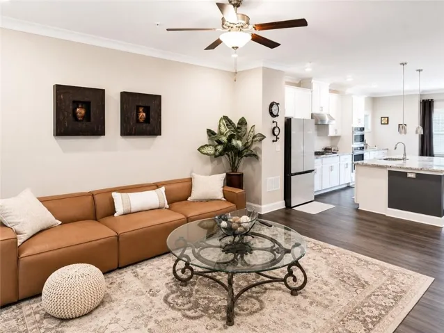 Open-concept living space featuring wood-finish flooring, a ceiling fan with light, and crown molding