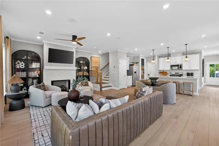 Open-concept living space featuring wood-finish flooring, a white brick fireplace, recessed lighting, a ceiling fan, and a kitchen with white cabinetry and pendant lighting