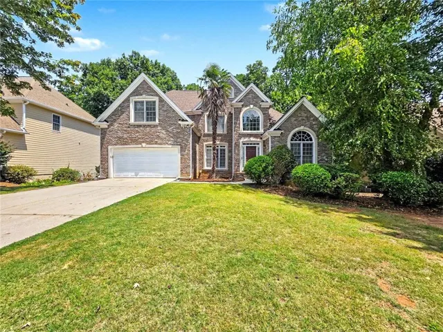 Brick Colonial-style residence featuring a two-car garage, arched entry portico with multi-pane windows, and peaked gable roofline