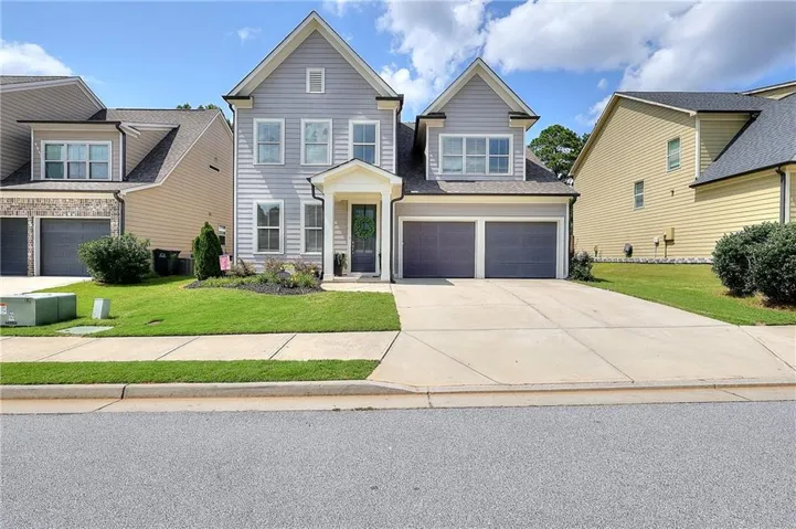 Two-story residence featuring light gray siding, a covered entry porch, and a two-car garage with dark gray doors