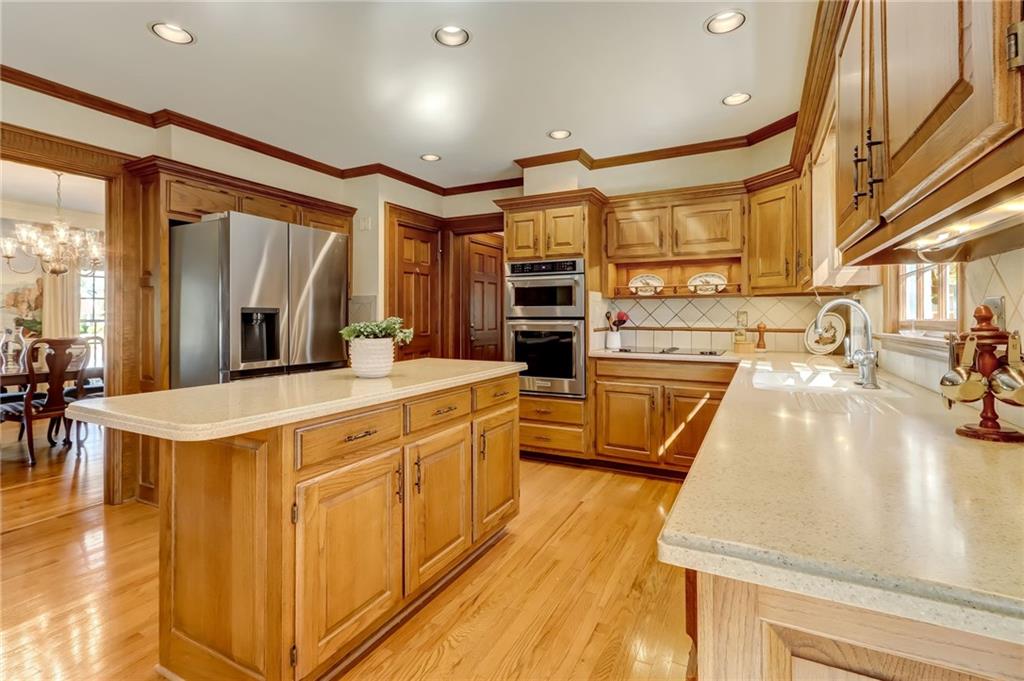 Kitchen with light wood-type flooring, an inviting chandelier, stainless steel appliances, light stone counters, and hanging light fixtures
