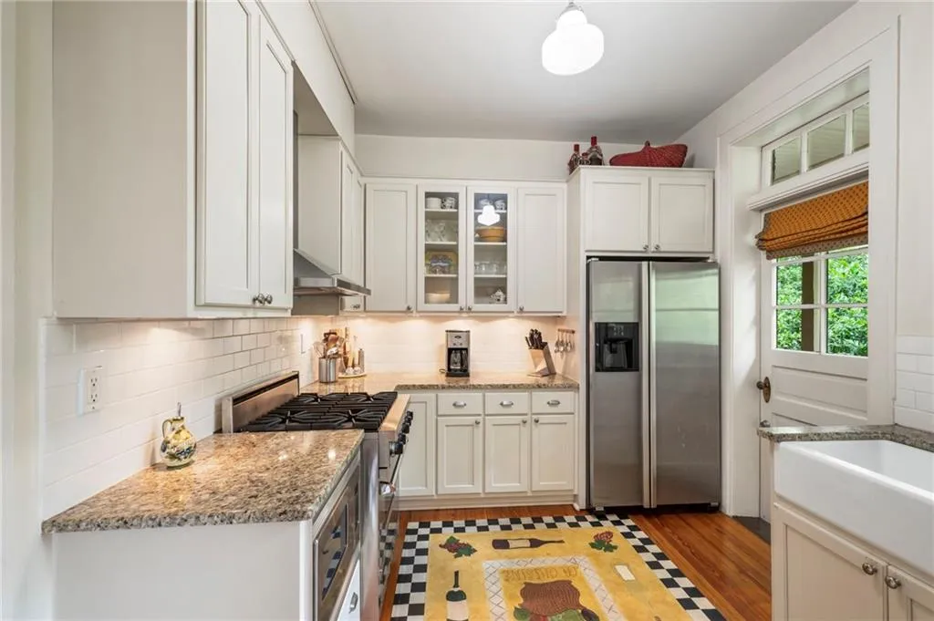 Kitchen with stainless steel appliances, glass insert cabinets, light stone counters, light wood-style flooring, and decorative backsplash