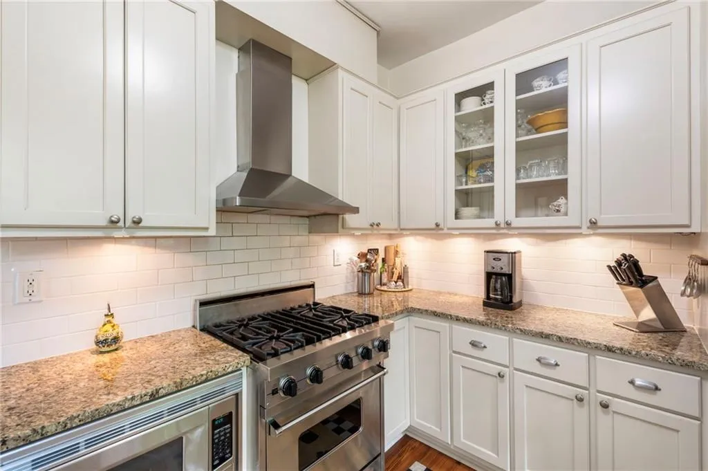 Kitchen featuring appliances with stainless steel finishes, wall chimney range hood, light stone counters, and decorative backsplash