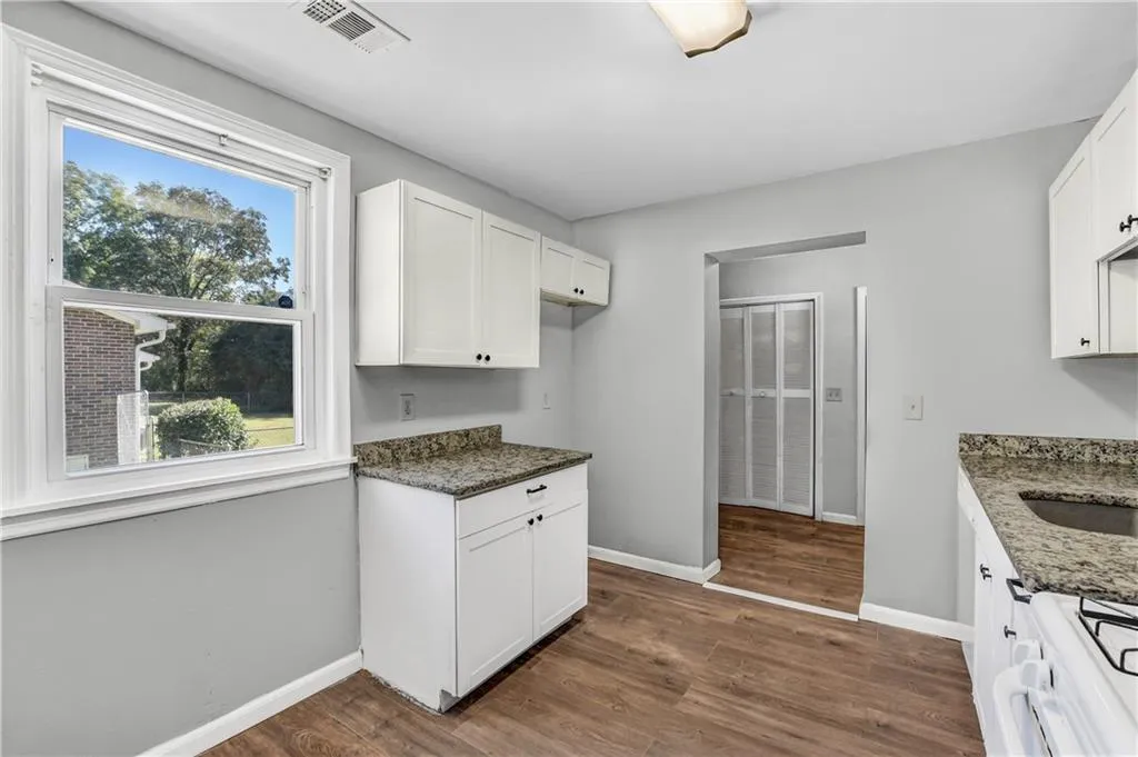Kitchen featuring dark stone countertops, white gas range, dark wood-style flooring, and white cabinets