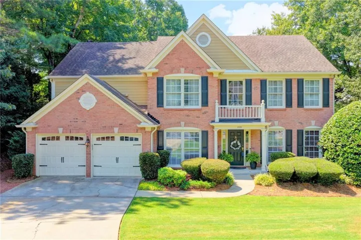 Brick exterior with siding accents, two-car garage with carriage-style doors, covered entry with a balcony, and a manicured front lawn