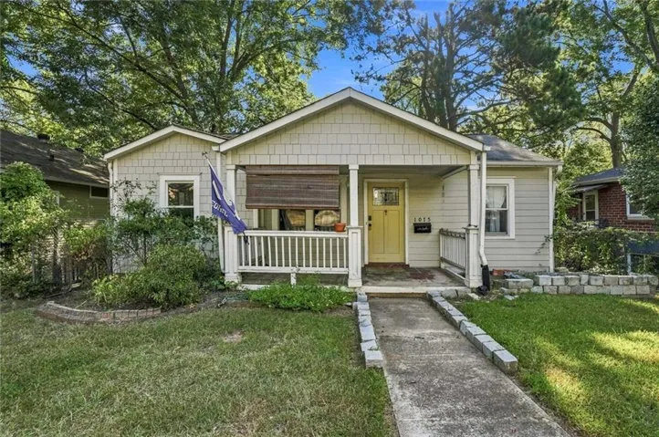 Gabled roofline, shingle siding, covered front porch, white porch railing, and concrete walkway
