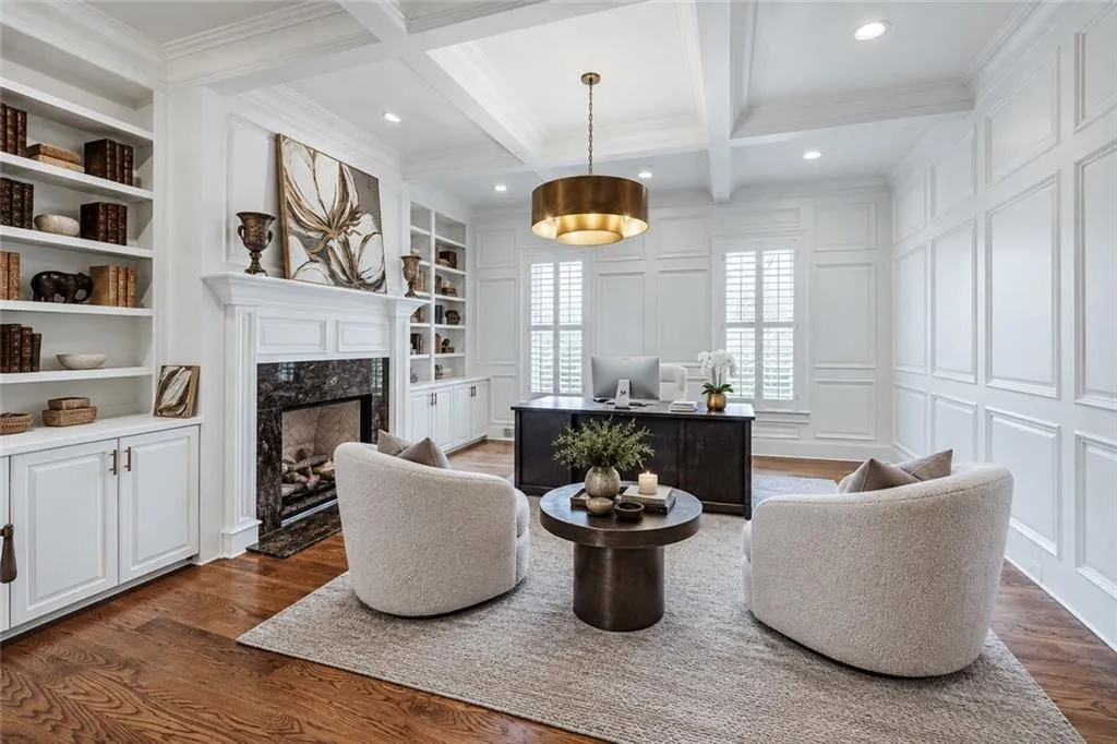 Coffered ceiling with recessed lighting, rich wood-finish flooring, built-in shelving, fireplace with stone surround, and paneled walls