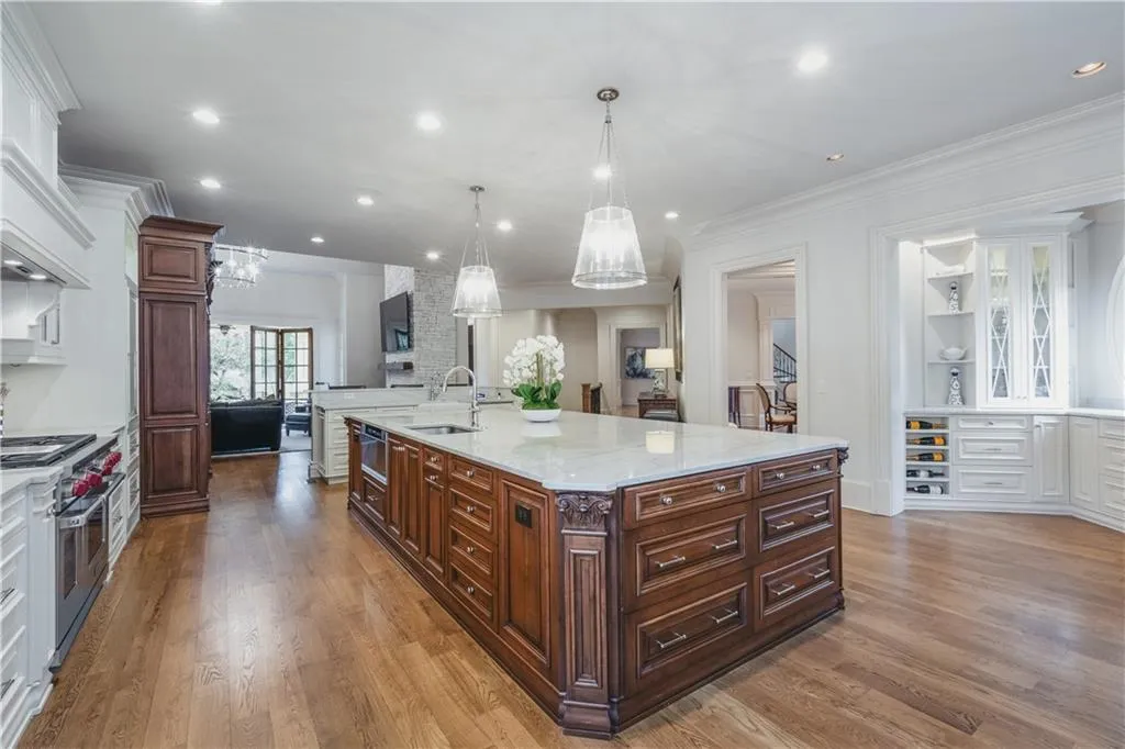 Spacious kitchen featuring a large central island with integrated storage, wood-finish flooring, recessed lighting, and built-in cabinetry with glass display doors
